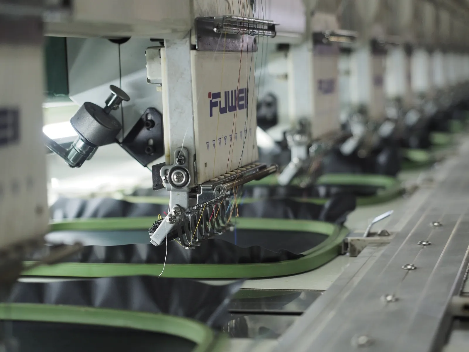 Multi-head embroidery machine stitching dark fabric held in green hoops