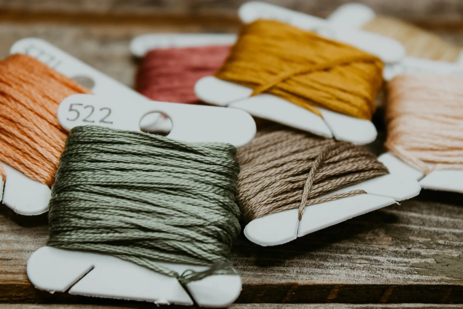 Skeins of embroidery floss in green, tan, gold, orange and pink wound on white bobbins
