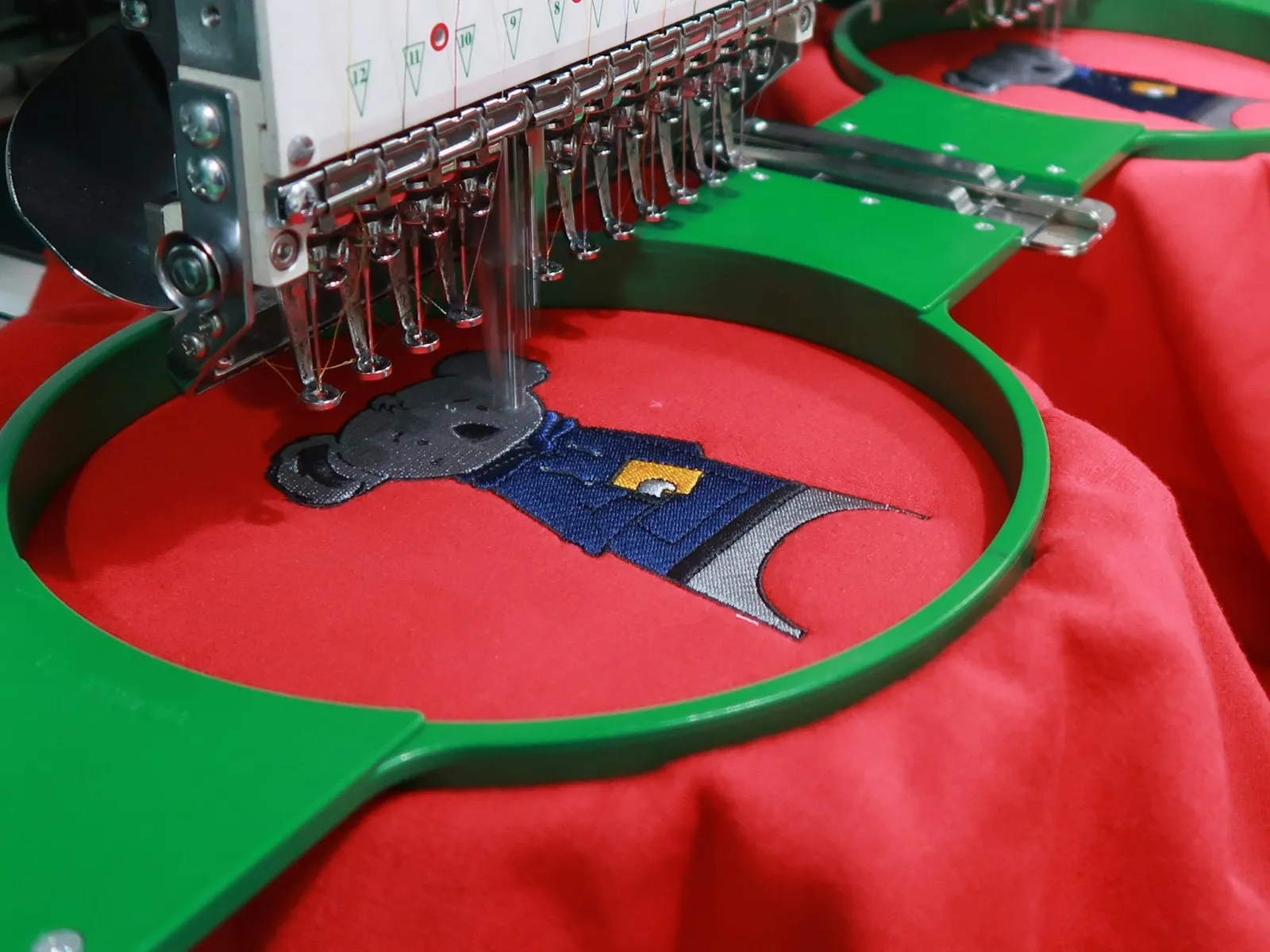 A multi-head embroidery machine stitching a design onto a red garment held in a hoop
