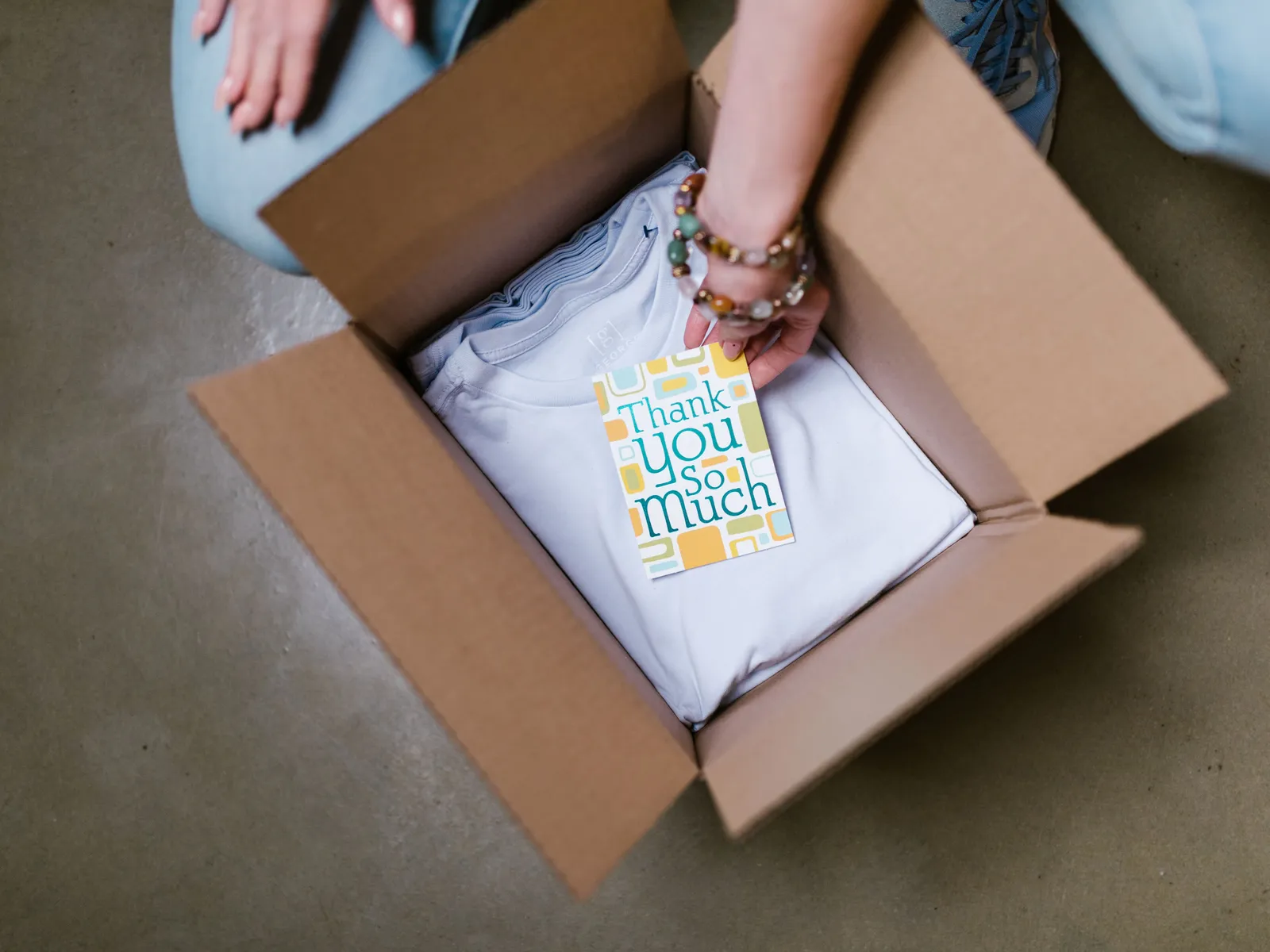 A folded t-shirt packed in a shipping box with a thank-you card on top