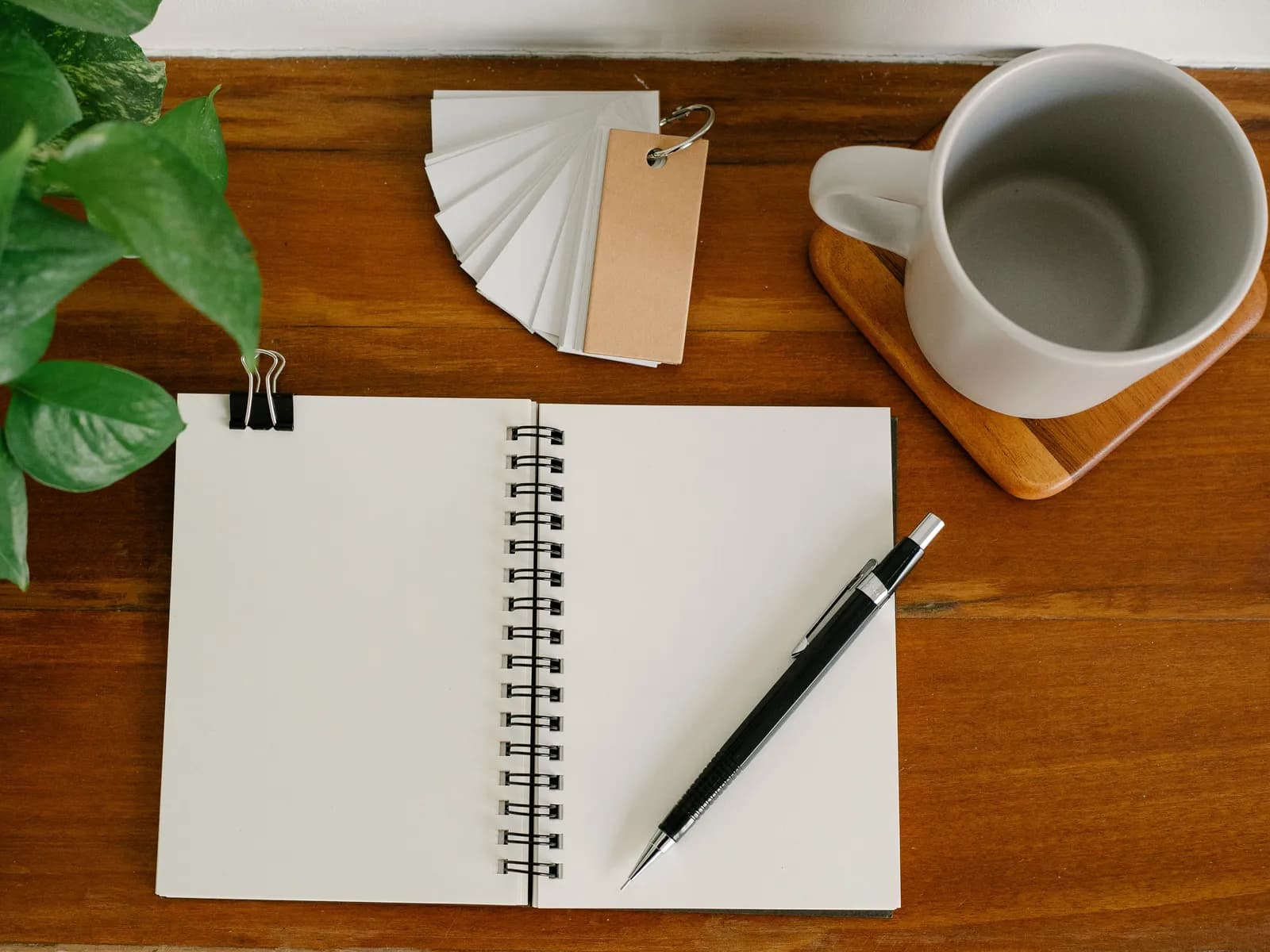 A blank spiral notebook, pen, mug and tag swatches on a wooden desk
