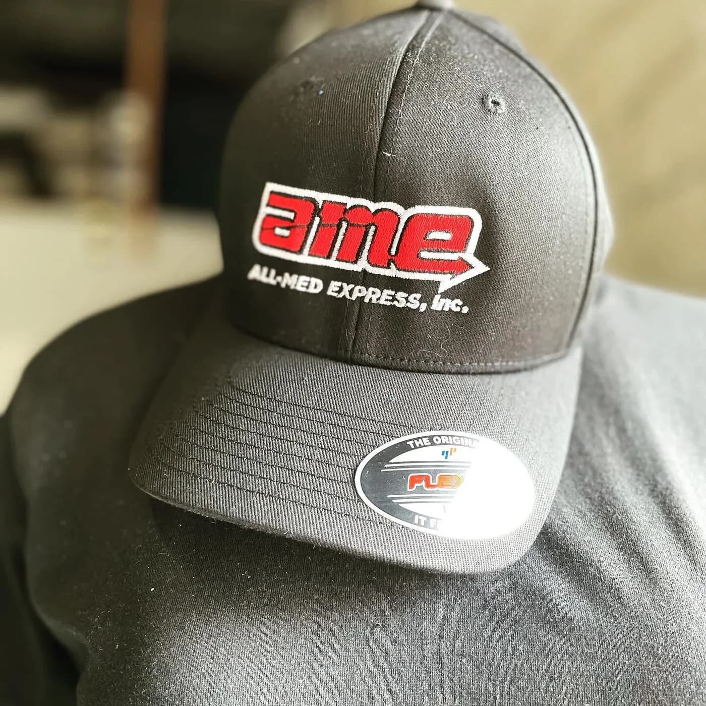 Black fitted cap with a red and white embroidered company logo on the front panel
