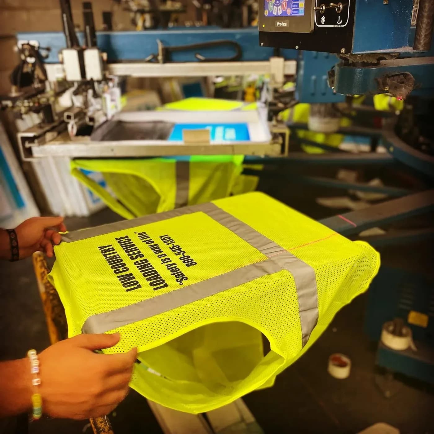 A yellow hi-vis safety shirt with reflective tape being pulled off the screen printing press